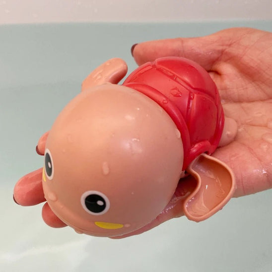 Une main tient le Baby BathToys™ - Jouets de bain pour bébé, un petit jouet rouge caricatural avec de grands yeux et une tête chauve - parfait comme jouets de bain sans pile pour les bébés.