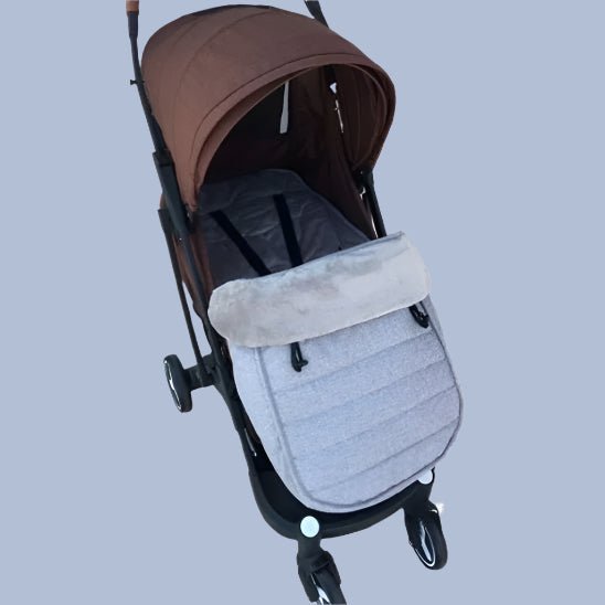 Une poussette marron avec capote et quatre roues est présentée sur un fond gris clair. À l'intérieur, des sangles de sécurité et la chancelière pour bébé WarmCott™ offrent une protection supplémentaire pour l'hiver.