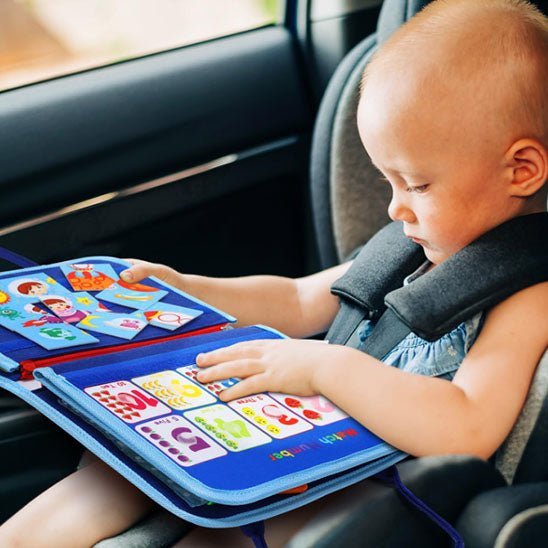 Un jeune enfant assis dans un siège de voiture explore le Livre d'activité - Jouet 2 ans, qui comporte des illustrations colorées et des chiffres, parfaits pour rendre l'apprentissage amusant pendant les déplacements.