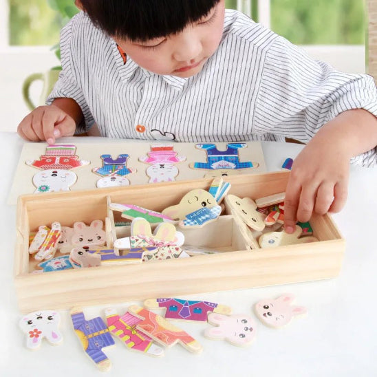 Un jeune enfant est assis à une table et joue avec le Puzzle dressing - Jouet bois, en arrangeant des pièces en forme de lapin et des tenues colorées dans ce jouet éducatif attrayant.