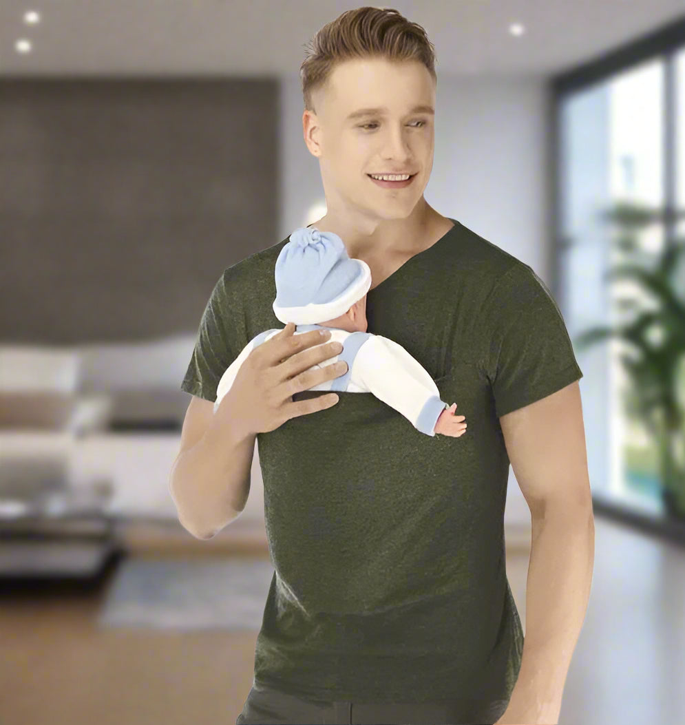 Un homme portant un T-shirt Porte Bebe vert foncé tient un bébé vêtu de vêtements bleus et blancs avec un chapeau assorti, souriant à sa gauche sur un fond blanc uni, une solution confortable pour les parents actifs.