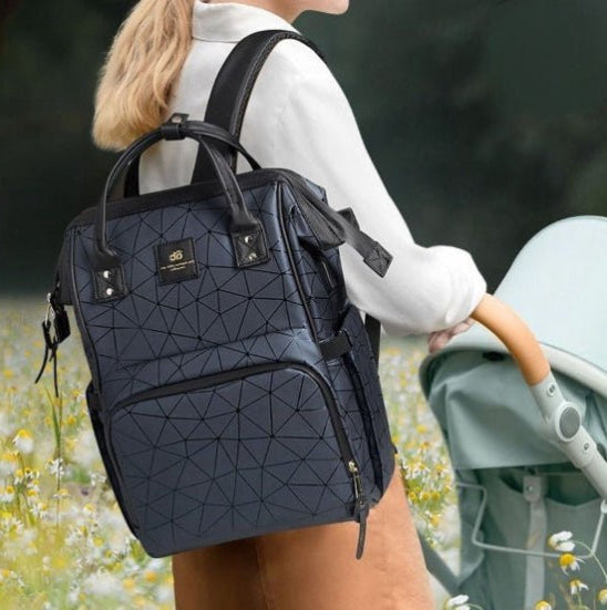 Une personne vĂȘtue d'une chemise blanche Ă manches longues porte le LifeEscapeâą Sac Ă Langer dos et pousse une poussette bleu clair, incarnant des parents modernes dans un champ rempli de fleurs sauvages.