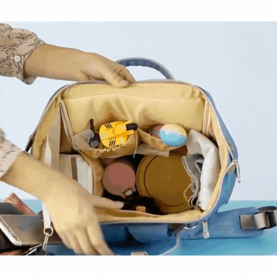 Une personne organise des jouets et des contenants à l'intérieur des compartiments d'un Sac a dos bebe | le Colorful ouvert sur une surface bleue.