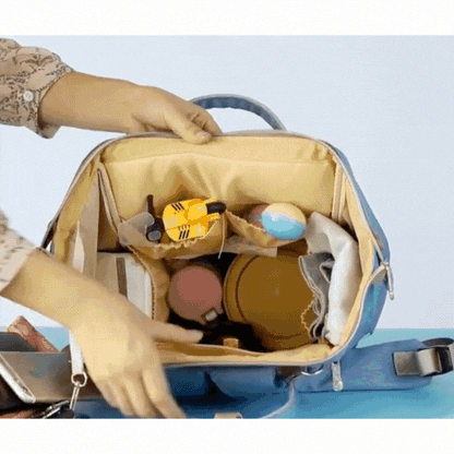 Une personne organise des jouets et des contenants à l'intérieur des compartiments d'un Sac a dos bebe | le Colorful ouvert sur une surface bleue.