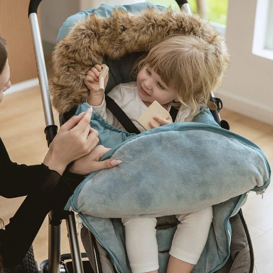 Un jeune enfant se détend dans une poussette avec une Chancelière bleue doublée de fourrure | 0-36 mois, jouant avec des blocs et souriant à un adulte qui tend la main pour lui donner un autre jouet.