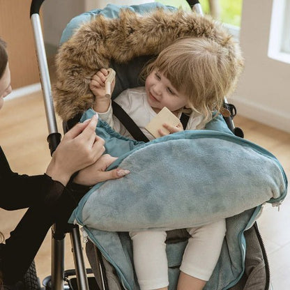 Un jeune enfant se détend dans une poussette avec une Chancelière bleue doublée de fourrure | 0-36 mois, jouant avec des blocs et souriant à un adulte qui tend la main pour lui donner un autre jouet.
