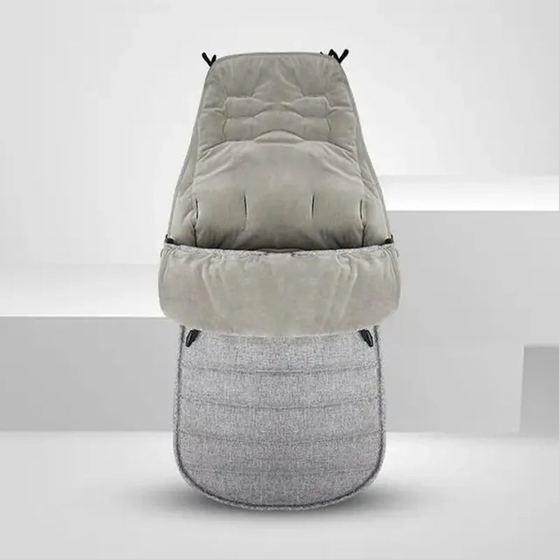 La Chancelière pour Poussette, présentée debout sur un fond clair uni, est confectionnée en tissu imperméable Oxford matelassé gris et offre douceur, isolation et protection fiable contre les intempéries à votre poussette.