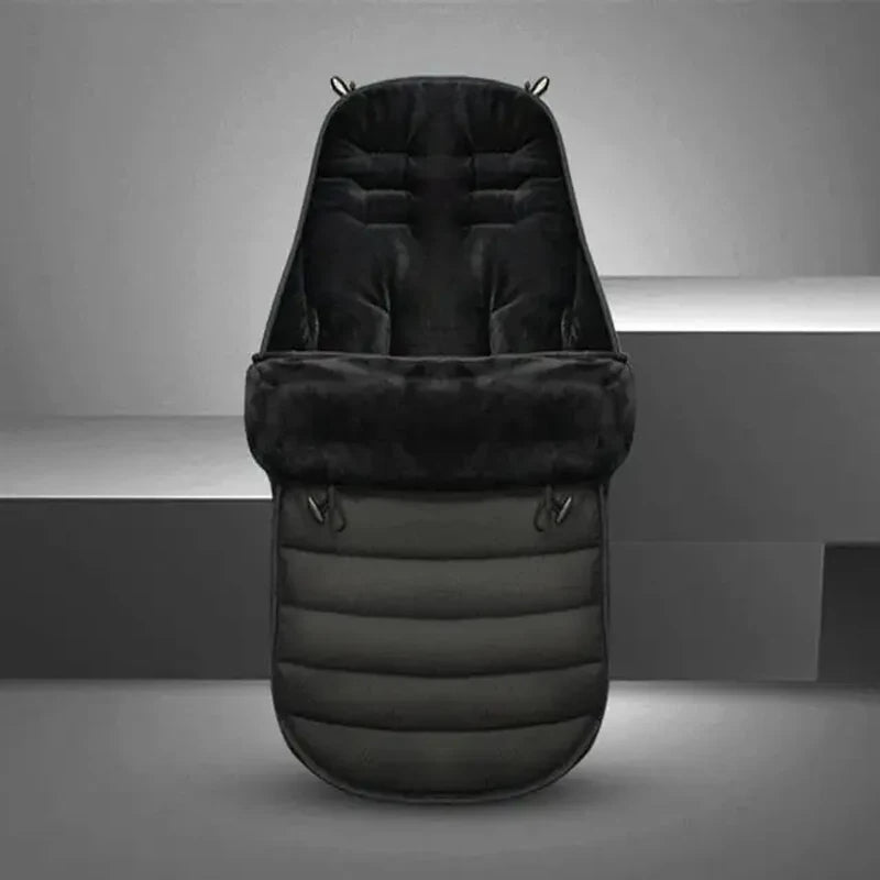 La Chancelière pour Poussette, présentée debout sur un fond gris minimaliste, présente un design rembourré noir avec une texture matelassée douce pour offrir protection contre les intempéries et confort à votre bébé.