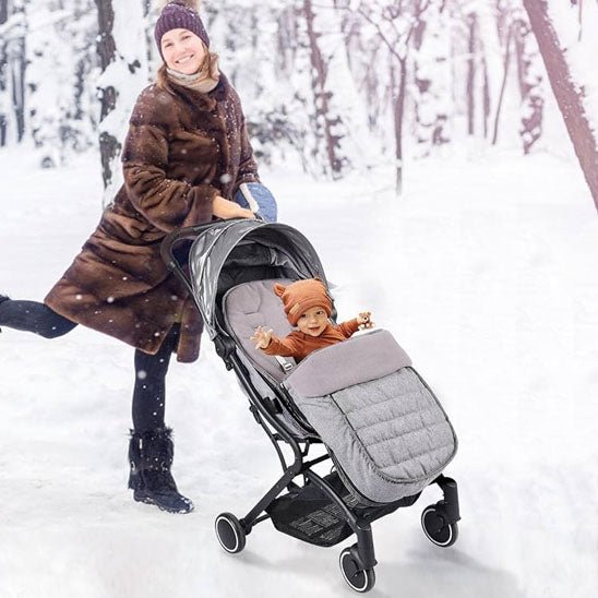 Une femme vêtue d'un manteau de fourrure marron pousse une poussette équipée de la Chancelière pour Poussette, gardant son bébé au chaud et protégé de la forêt enneigée grâce à son tissu Oxford imperméable et à son excellente protection contre les intempéries.