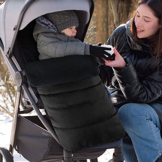 Une femme tend un objet à un enfant dans une poussette. L'enfant reste au chaud et protégé à l'extérieur dans une Chancelière pour Poussette en tissu Oxford imperméable, tout en portant un manteau d'hiver et un bonnet.