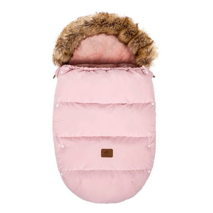 La Chancelière Poussette | 0-24 mois est une chancelière de poussette rose de forme ovale avec des coutures matelassées et une capuche bordée de fausse fourrure pour la protection thermique, ainsi qu'un petit patch marron sur le devant pour le confort de bébé, présentée sur un fond blanc.