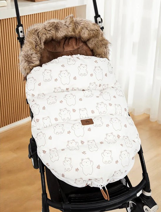 La Poussette Chancelière | Hiver 0-24 mois, au motif ours blanc et beige avec doublure en fausse fourrure pour le confort de bébé et sa protection thermique, est présentée en intérieur sur un parquet près de rideaux blancs et d'un mur lambrissé.