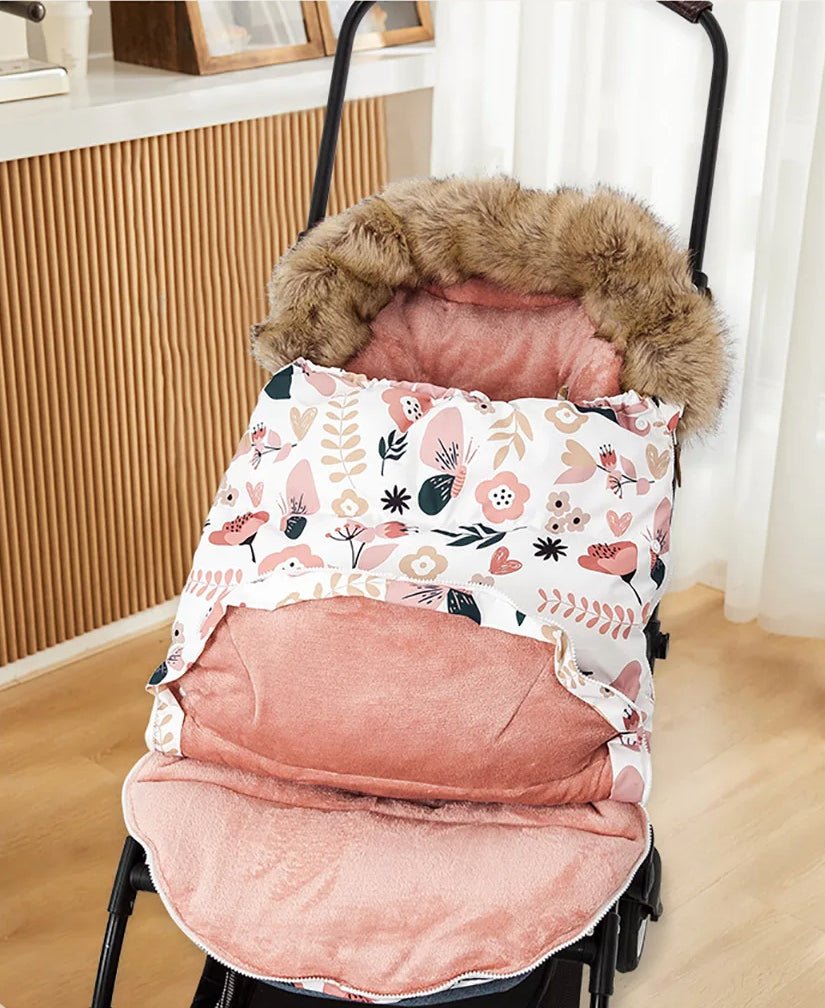 La Poussette Chancelière | Hiver 0-24 mois, au motif floral et bordée de fourrure rose, blanc et beige, est posée sur un plancher en bois près d'une fenêtre avec des rideaux transparents, offrant confort bébé et protection thermique.