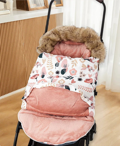 La Poussette Chancelière | Hiver 0-24 mois, au motif floral et bordée de fourrure rose, blanc et beige, est posée sur un plancher en bois près d'une fenêtre avec des rideaux transparents, offrant confort bébé et protection thermique.