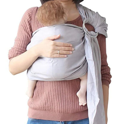 Une femme vêtue d'un pull côtelé à manches longues berce son bébé dans l'Echarpe portage bébé | RingSling™, tenant le bébé vers l'intérieur pour un contact peau à peau apaisant et le soutenant doucement d'une main.