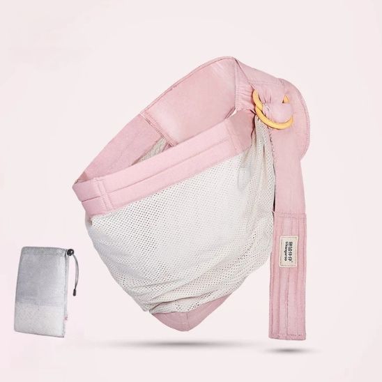 Une écharpe de portage rose Echarpe | SwaddleSling™, dotée d'une poche en filet et d'un anneau de réglage doré, est présentée à côté d'une petite pochette à cordon grise sur un fond clair uni.