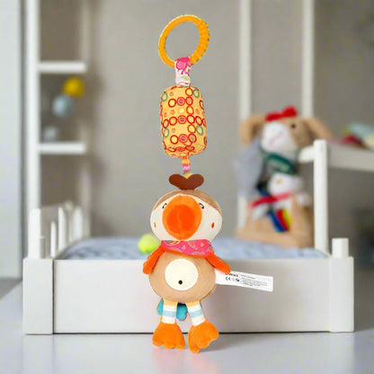 Le Jouet - Hochet Bébé, un oiseau en peluche au bec et aux pattes orange, est suspendu à un anneau comme un charmant jouet d'éveil dans une chambre d'enfant avec un berceau et des animaux en peluche flous en arrière-plan.