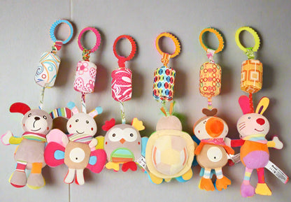 Sept peluches colorées Jouet - Hochet Bébé, chacune avec un dessin d'animal unique, sont suspendues à des cylindres et des anneaux en tissu à motifs, idéaux pour stimuler l'éveil sensoriel de bébé, sur un fond gris clair uni.