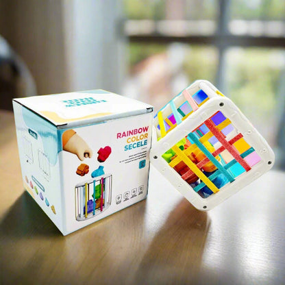 Un cube en plastique de Jeux d'eveils - cubes éducatifs, aux formes géométriques et aux bandes arc-en-ciel, est posé sur une table en bois, idéal pour le jeu des tout-petits et le développement des bébés.