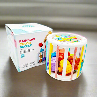 Un jouet sensoriel cylindrique coloré rempli de blocs façonnés est posé à côté de sa boîte étiquetée "Jeux d'éveils - cubes éducatifs", un jeu d'éveil idéal conçu pour le développement des bébés.