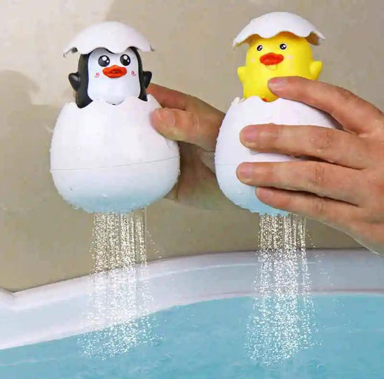 Deux mains tiennent un œuf en plastique « Jouet de bain » avec un pingouin et un poussin à l'intérieur. L'eau s'écoule de chaque jouet dans la baignoire, pour une expérience ludique et la sécurité de l'enfant.