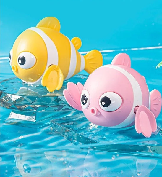 Deux jouets de bain – des poissons nageurs, l'un jaune rayé de blanc et l'autre rose rayé de blanc – sont posés sur une surface bleue semblable à de l'eau. Avec leurs grands yeux et leurs nageoires de dessin animé, ils sont parfaits pour le bain de bébé.