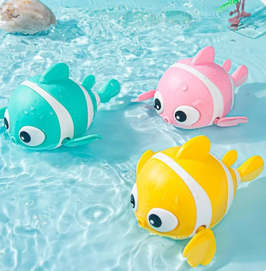 Trois poissons-jouets colorés – un bleu sarcelle, un rose et un jaune – flottent sur une eau bleu clair. Avec leurs yeux et leurs nageoires de dessin animé, ils sont parfaits pour rendre la baignade de bébé amusante et ludique.