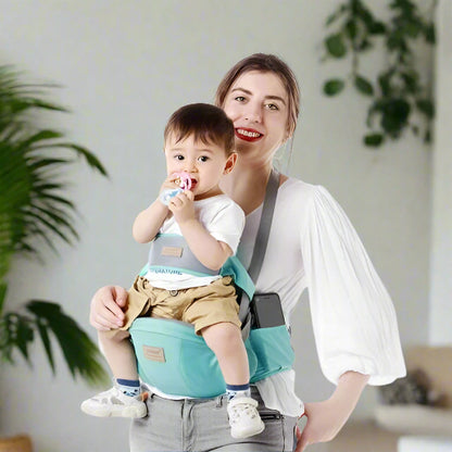 Une femme sourit en tenant un bébé dans le porte-bébé Porte Bébé | WaistHolder™, qui offre un confort ergonomique. Le bébé, vêtu d'une chemise blanche et d'un short kaki, tient une tétine. Des plantes vertes et un fond clair complètent la scène.