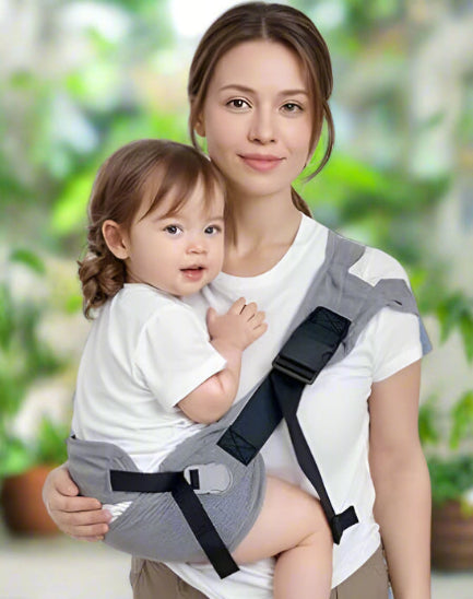 Une femme en chemise blanche porte un tout-petit HandsFree sur sa hanche dans le Porte Bébé - HandsFree gris, tous deux face à la caméra avec un fond vert doux, idéal pour les parents actifs.
