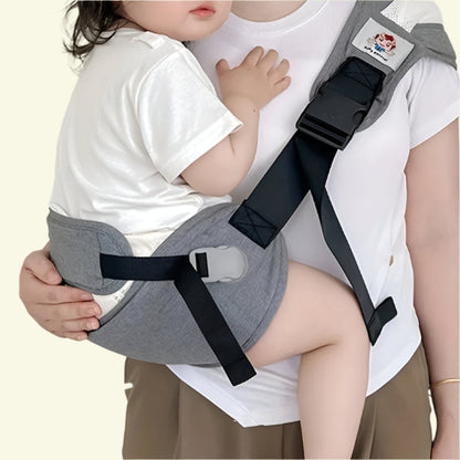 Un parent actif porte une chemise blanche et porte son enfant les mains libres sur sa hanche à l'aide du Porte Bébé - HandsFree, un porte-bébé gris avec des sangles et une boucle noires ; le bras de l'enfant repose doucement sur la poitrine du parent.