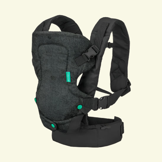 Un Porte Bebe physio noir et gris foncé | FlipAdvanced™ avec des sangles rembourrées, des boucles réglables et des boutons d'accent vert est présenté sur un fond blanc cassé uni, soulignant son confort ergonomique et polyvalent.