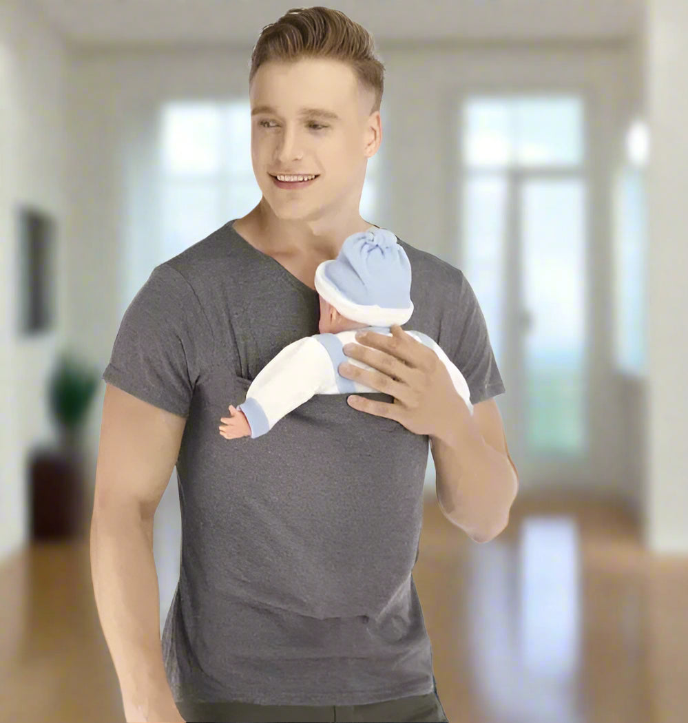 Un homme portant un T-shirt Porte Bebe gris tient une poupée bébé bleue et blanche sur son épaule, présentant cette solution confortable pour les parents actifs sur un fond blanc uni.