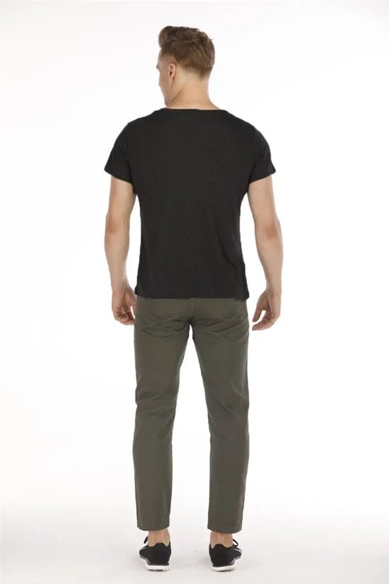 Un homme, dos à la caméra, porte un t-shirt noir Porte-Bébé, un pantalon vert olive et des chaussures noires : une solution confortable pour les parents actifs. Le fond est blanc uni.