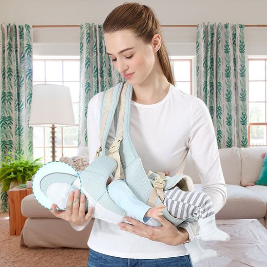 Une femme en chemise blanche utilise un Porte Bebe WaistStool™ bleu clair pour tenir et nourrir son bébé dans un salon avec des rideaux à motifs, une plante en pot et une lampe, assurant sécurité et confort pour les deux.