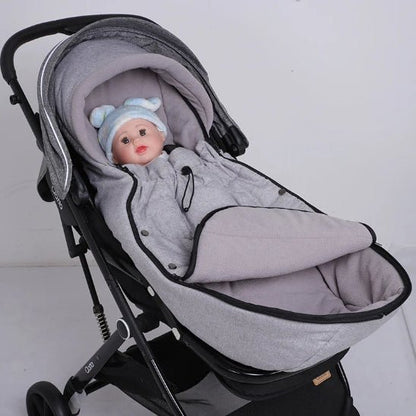 Un bébé vêtu d'une combinaison grise avec un chapeau bleu et blanc est allongé dans la Poussette Chancelière, qui offre une protection thermique, sur un fond blanc uni.