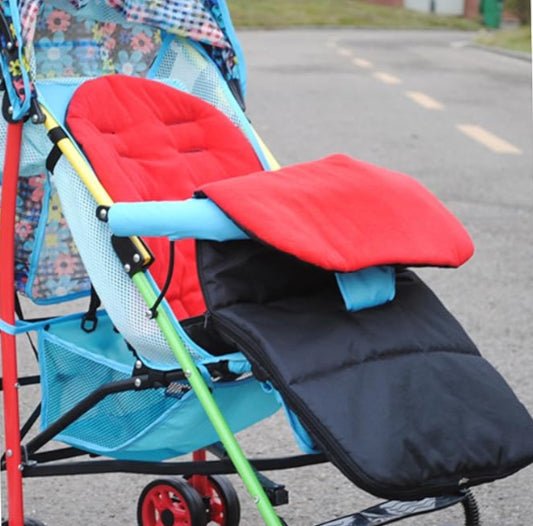 La Poussette Chancelière | CosyToes™ est dotée d'un auvent fleuri, d'un rembourrage de siège rouge, d'une chancelière noire et d'un cadre aux accents bleus, jaunes et verts, offrant un confort hivernal élégant sur un chemin extérieur vide.