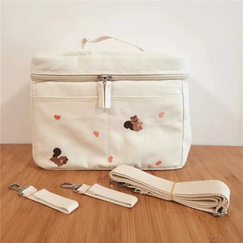 Le Sac à Langer Bébé est un sac à langer de couleur crème doté d'une fermeture à glissière et d'adorables motifs d'écureuil et de gland, présentés sur une surface en bois avec deux sangles amovibles plus une bandoulière pour plus de fonctionnalité et de style.