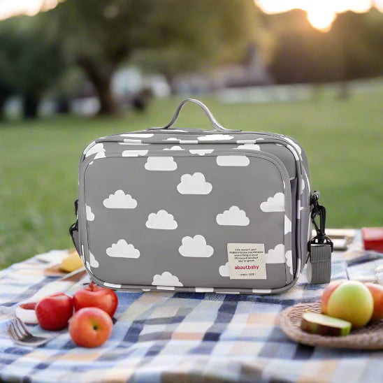 Le Sac à langer bébé | Poussette est un sac à langer rectangulaire gris avec un motif de nuages blancs, une poignée supérieure, une poche avant zippée, une bandoulière amovible et une étiquette « à propos de bébé » - idéal pour organiser les accessoires de bébé en déplacement.