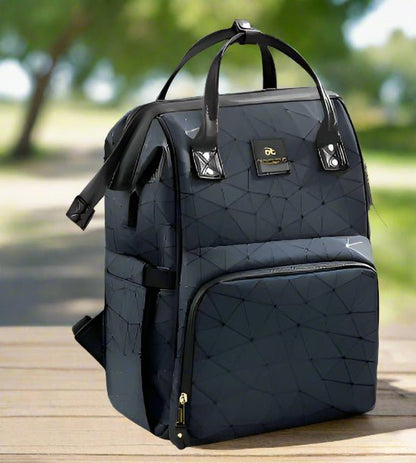 Le Sac a Langer dos | LifeEscape™ en noir avec un motif géométrique, des poignées courtes et des sangles réglables repose sur du bois à l'extérieur - un compagnon de voyage idéal pour les parents modernes, avec des arbres et un chemin doucement estompés derrière.