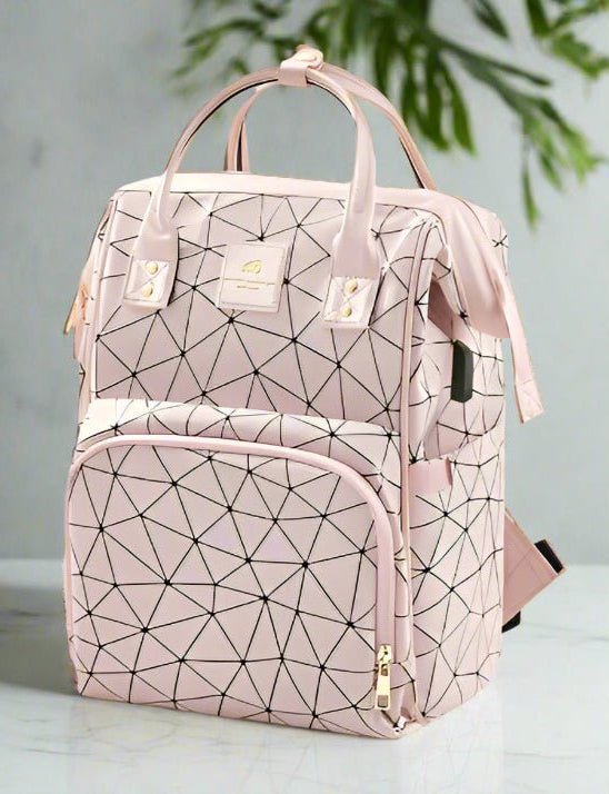 Le Sac a Langer dos | LifeEscape™ est un sac à dos à couches rose pâle avec des lignes géométriques noires, des fermetures éclair dorées, une poche frontale zippée et deux poignées supérieures sur une surface blanche - idéale pour les parents modernes - avec des feuilles vertes en arrière-plan.