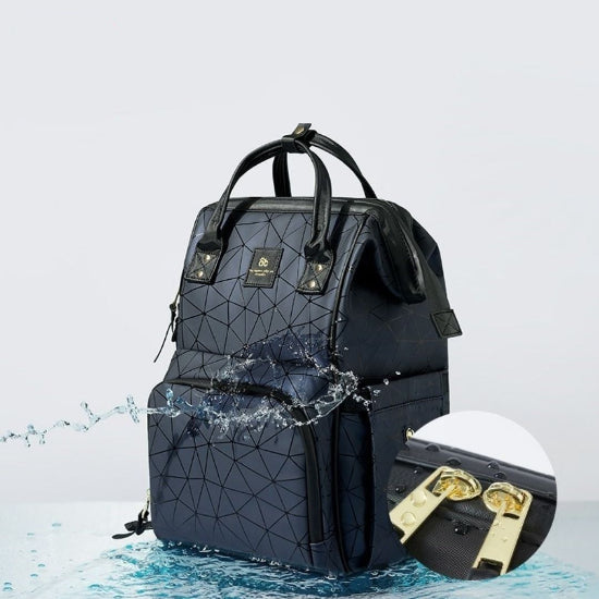 Le Sac à Langer dos, un sac à dos noir à motifs géométriques, est présenté sur un fond clair avec des éclaboussures d'eau pour souligner sa résistance à l'eau. Parfait pour les parents modernes, un insert met en valeur deux tirettes de fermeture éclair dorées, un essentiel élégant pour les sorties en famille.