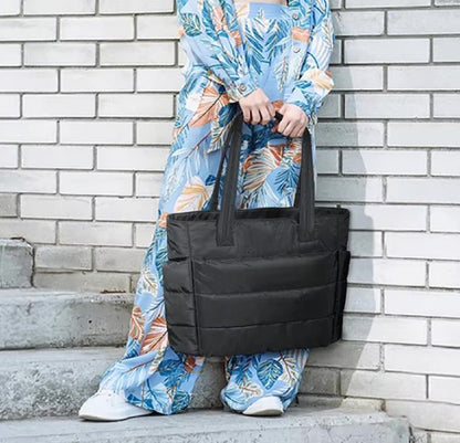 Une personne vêtue d'une tenue bleue à motifs de feuilles colorées se tient sur les marches d'un mur de briques blanches, tenant le Sac à langer | Maman. Son visage est invisible.