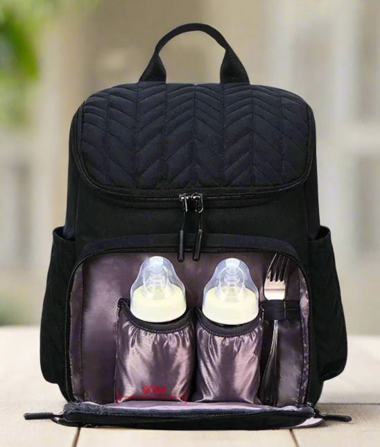 Un Sac Bebe à Langer - NappyBag a dos noir, dont la poche avant est ouverte, révèle deux biberons dans des supports isothermes et une fourchette en métal dans une fente latérale, présentés sur une surface de couleur claire.