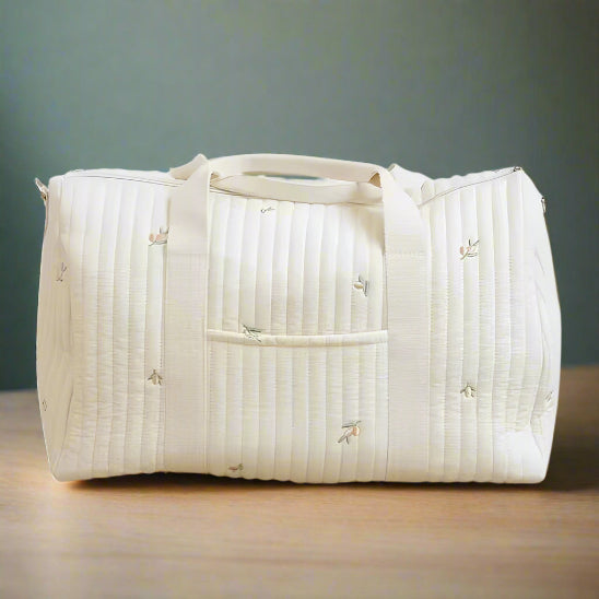 Le Sac bébé à Langer | Maternité est un sac rectangulaire matelassé crème avec deux poignées, une bandoulière, une poche avant et de délicates fleurs brodées, idéal pour les mamans en déplacement ou pour les besoins de maternité.