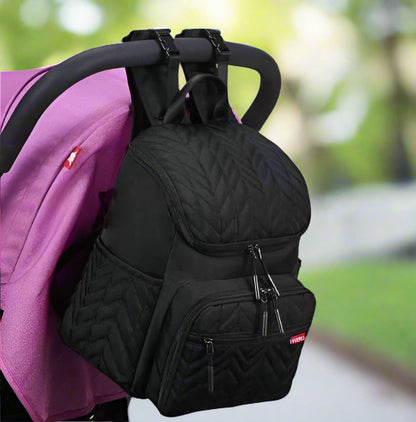 Le Sac Bebe à Langer - Nappy, avec son motif matelassé noir et ses bretelles réglables, pend élégamment du guidon dune poussette violette. Il offre plusieurs compartiments zippés pour une combinaison parfaite délégance et de fonctionnalité lors de vos sorties.