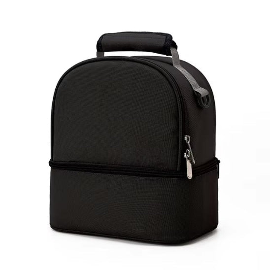 Le Sac Bébé - Petit est un sac à lunch noir rectangulaire aux bords arrondis, doté d'une poignée sur le dessus et de deux compartiments pour une organisation facile. Sa performance thermique préserve la fraîcheur des aliments, présenté debout sur un fond blanc uni.