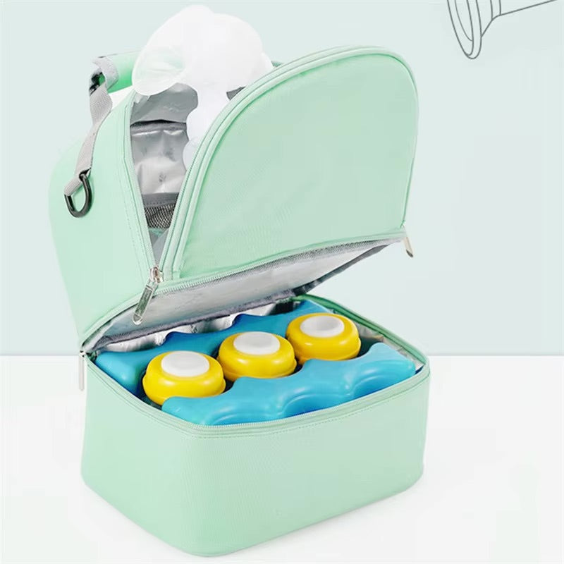 Le Sac Bébé - Petit, un sac à lunch isotherme vert menthe à deux compartiments, s'ouvre pour révéler des couvercles bleus et jaunes et un tissu blanc à l'intérieur. Profitez de sa performance thermique fiable sur fond vert clair.