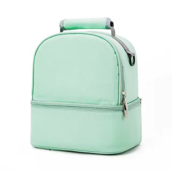Le Sac Bébé - Petit est un sac bébé vert clair doté de deux compartiments, d'une poignée supérieure et de deux fermetures éclair. Présenté sur un fond blanc uni, il offre une performance thermique optimale pour conserver la fraîcheur des repas.