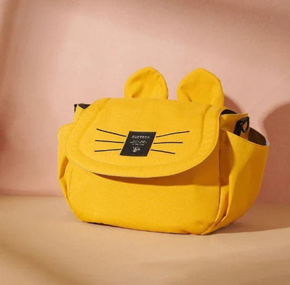 Le Sac bébé - Poussette, un sac jaune aux détails de moustaches noires et de petites oreilles, est présenté sur un fond beige. Conçu comme un accessoire pratique, il est doté dune fermeture à rabat et dune étiquette rectangulaire noire sur le devant. Idéal pour organiser les essentiels lors de vos déplacements.