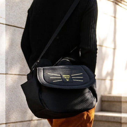 Une personne en haut noir porte un élégant sac bébé noir avec des coutures jaunes. Dos à la caméra, elle se tient près dun vieux mur de pierre et de marches.